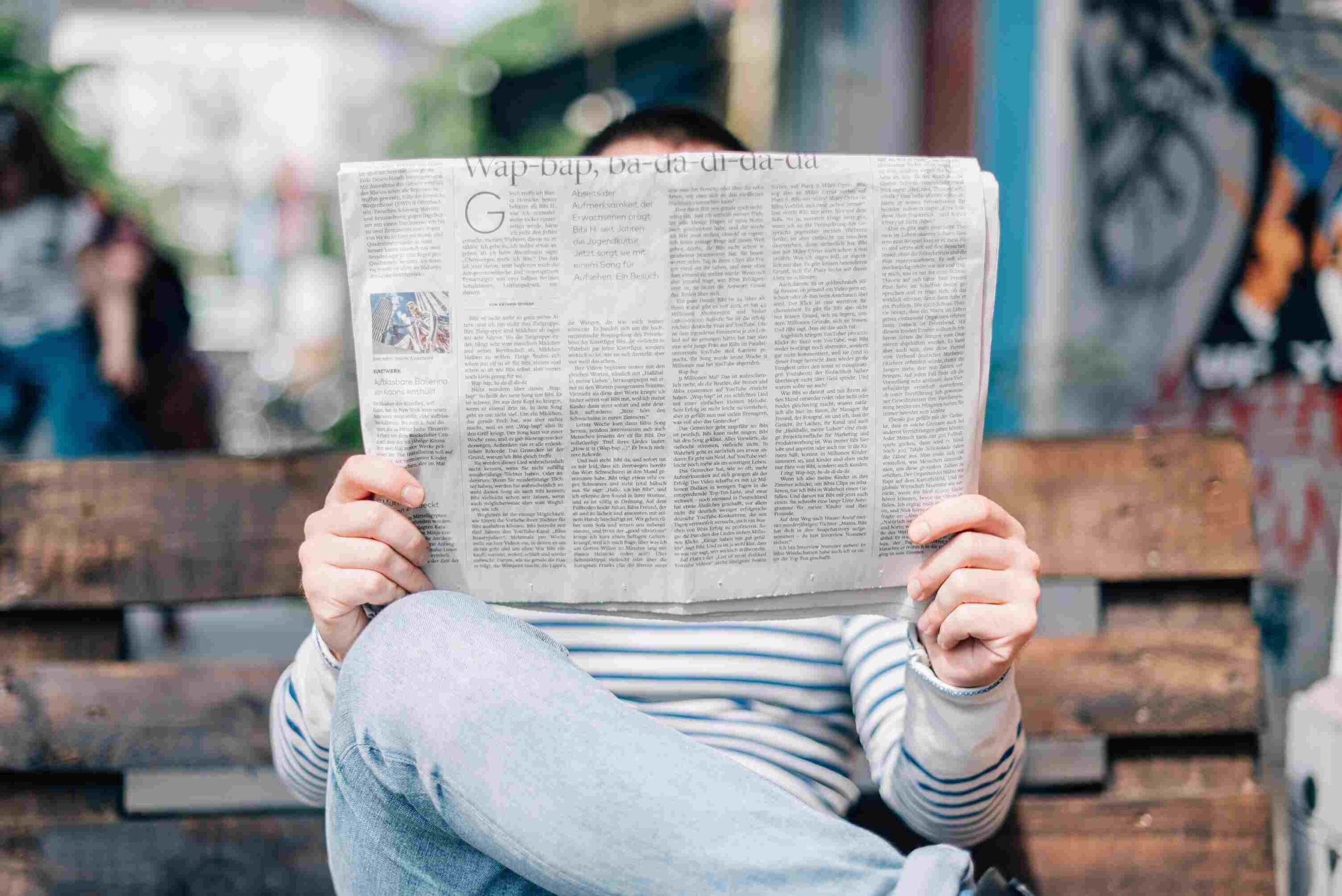 person holding newspaper reads about current events